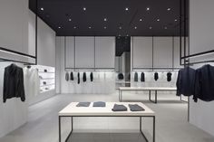 an empty clothing store with white walls and black clothes hanging on the racks in front of them