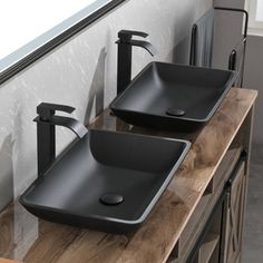 two black bathroom sinks sitting on top of a wooden counter