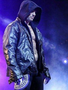 a man in black leather jacket and hoodie standing on stage with his hands in his pockets