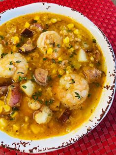 a white bowl filled with shrimp and corn soup on top of a red place mat