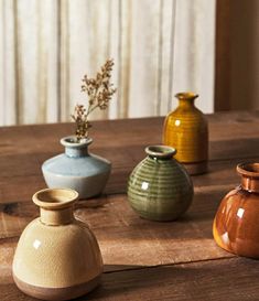 four vases sitting on top of a wooden table next to each other, all different colors