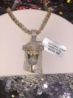 a necklace with a gold jesus head on it and a tag attached to the chain