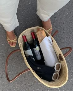 a person standing next to a basket filled with wine bottles and other items on the ground