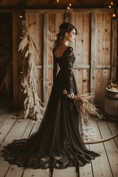 a woman in a long black dress standing on a wooden floor next to a barrel