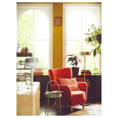 an orange chair sitting in front of two windows next to a potted plant and table