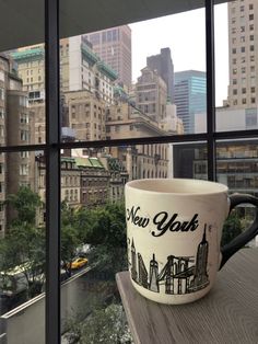 a coffee cup sitting on top of a window sill in front of a cityscape