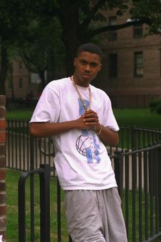 a young man standing next to a black fence in front of a brick building and green grass