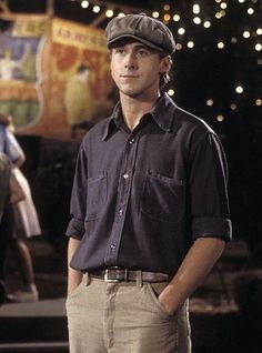 the young man is wearing a hat and standing in front of some christmas lights with his hands on his hips