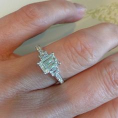 a woman's engagement ring with an emerald cut diamond in the center, on her finger