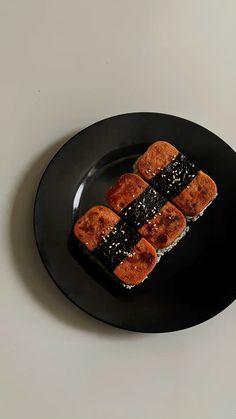 three pieces of sushi on a black plate sitting on a white table top next to a knife and fork