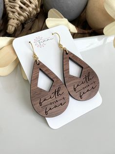 wooden earrings with the words faith is what you want to hear on them, sitting next to some flowers