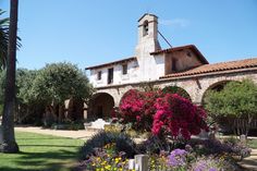 an old building with flowers in the front yard and palm trees on the other side