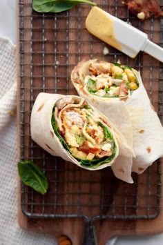 two burritos sitting on top of a cutting board next to cheese and spinach