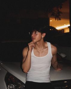 a young man leaning on the hood of a car at night with his hand under his chin