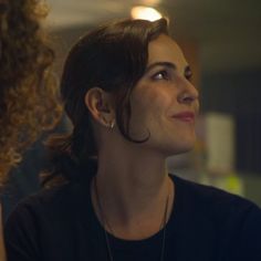 a woman with curly hair and piercings looks up into the sky while standing in front of another woman