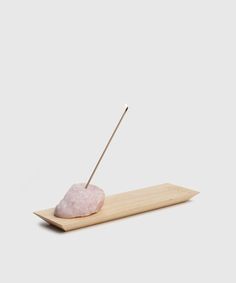 a pink rock with two sticks sticking out of it sitting on a wooden tray next to a white wall