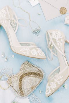 wedding shoes and jewelry laid out on a blue tablecloth with white lace, brooches, and pearls