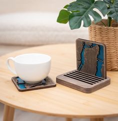 a cup and saucer sitting on top of a wooden table next to a plant