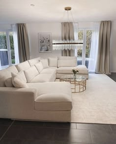 a living room filled with furniture and a chandelier hanging from the ceiling in front of two windows