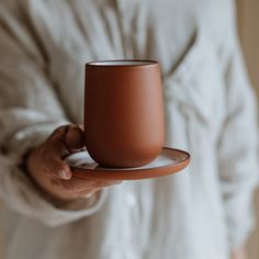 a person holding a brown cup and saucer in their left hand while wearing a white shirt