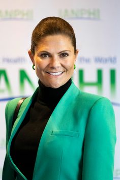 a woman in a green jacket and black top smiles at the camera while posing for a photo