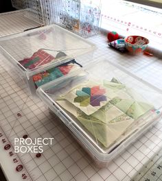 two plastic containers with quilts in them sitting on a cutting board next to scissors