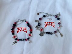 two bracelets with red and black beads are on a white sheet that is laying on a bed