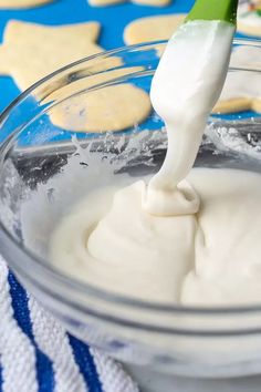 a glass bowl filled with white icing next to cookies on a blue and white towel