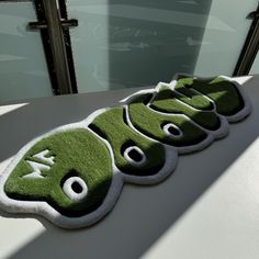 three green rugs with eyes on them sitting on top of a white table next to a window