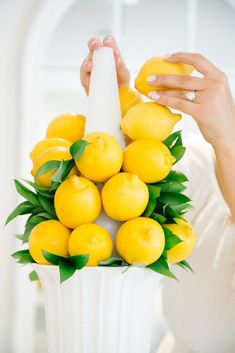 a woman holding a white vase filled with lemons