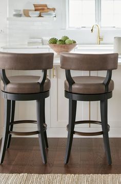 two brown stools sitting in front of a counter top with a bowl of fruit on it