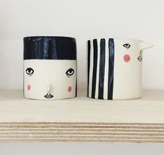 two coffee mugs sitting on top of a shelf next to each other with faces painted on them