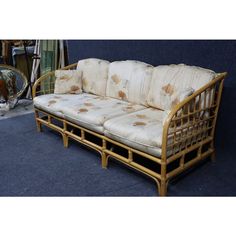 a rattan couch with cushions on it in front of a blue carpeted floor