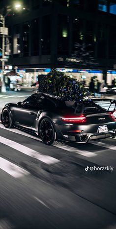 a black sports car with a christmas tree on its roof driving down the street at night