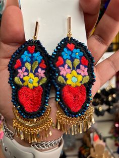 a pair of earrings with flowers and chains on them are being held up by someone's hand