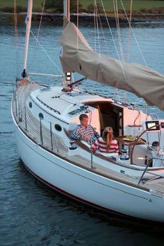 a man and woman are sitting on the deck of a sailboat in the water