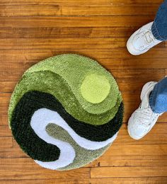 a person standing on a wooden floor next to a green and white rug with an oval design