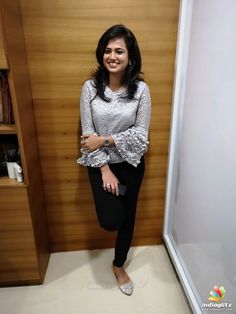 a woman standing in front of a wooden wall with her hands on her hips and smiling at the camera