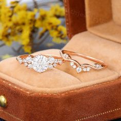 two engagement rings sitting in a box on top of a piece of leather with yellow flowers behind them