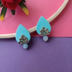 a pair of blue earrings sitting on top of a purple table next to a pink flower