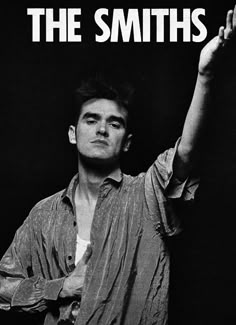 a man holding his hand up in the air while standing next to a black background