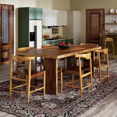 a kitchen with an island table surrounded by stools and chairs in front of a refrigerator