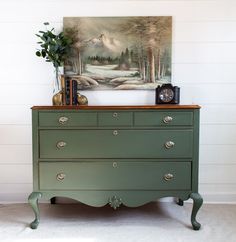 a green dresser with a painting on the wall behind it