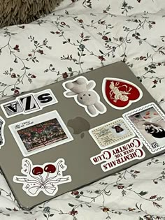 an open laptop computer sitting on top of a bed covered in stickers and decals