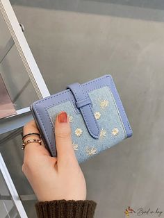 a woman's hand is holding a blue wallet with flowers on the front and sides