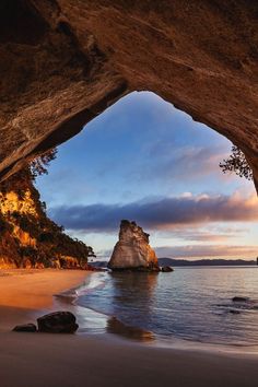 an ocean cave with the sun setting behind it and rocks in the water at the beach