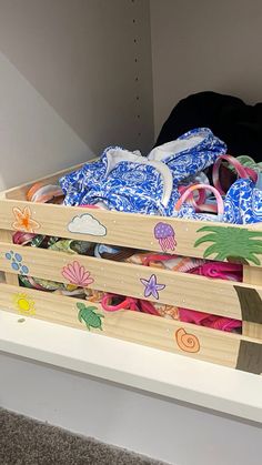 a wooden crate filled with clothes on top of a carpeted floor next to a white wall