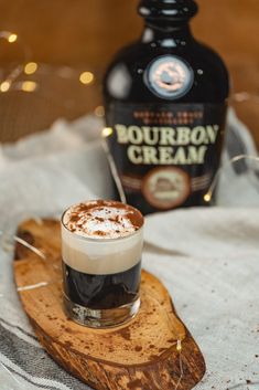 a drink sitting on top of a wooden tray next to a bottle of bourbon cream