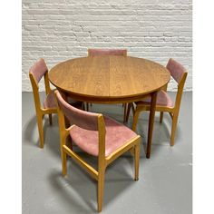 a wooden table with pink chairs around it and a white brick wall behind the table