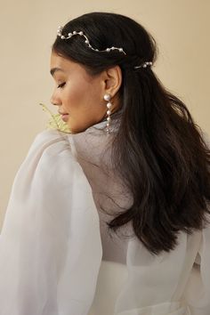 a woman with long hair wearing a white blouse and pearls in her hair is looking off to the side